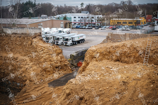 Construction pit with visible geological layers and nearby cement trucks in Luxembourg