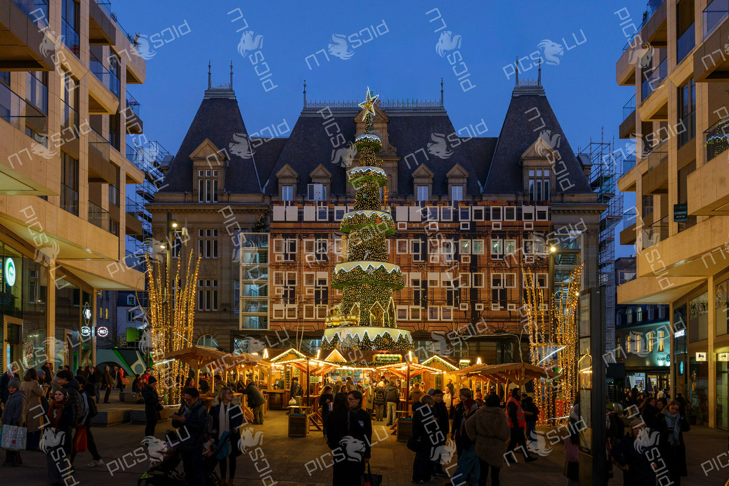 Illuminated Christmas tree and wooden stalls at a Christmas market in a city square in Luxembourg