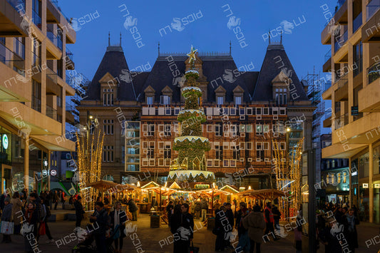Illuminated Christmas tree and wooden stalls at a Christmas market in a city square in Luxembourg